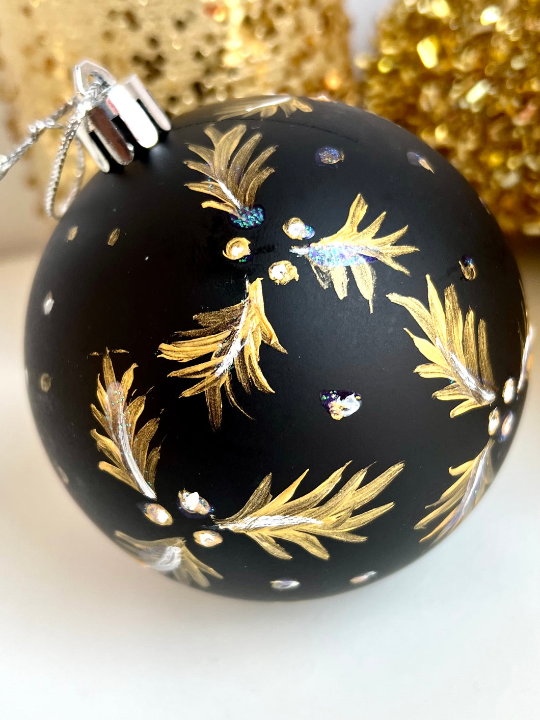 Black Christmas ornament hand painted with gold and white holly leaves and berries